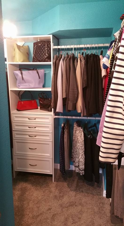 A walk-in closet with white shelving, five drawers, and two hanging rods filled with clothes against teal walls.