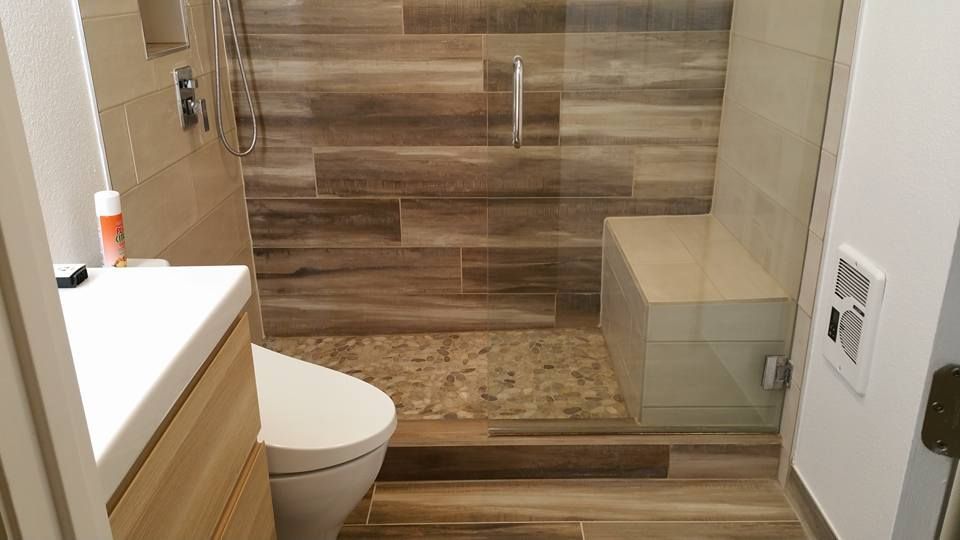 A modern bathroom featuring a walk-in shower with wood-look tile walls, a stone-tiled floor, a glass partition, and a bench.