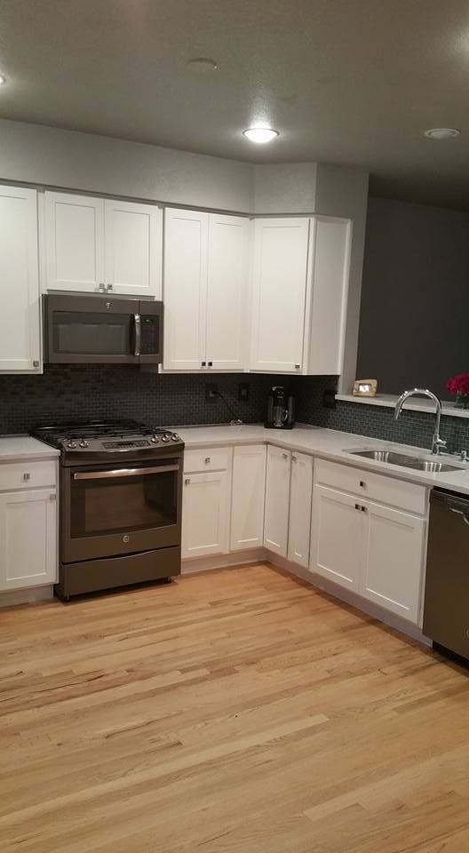 A kitchen with white cabinets, dark countertops, a dark stainless steel oven and microwave, and light wood flooring.