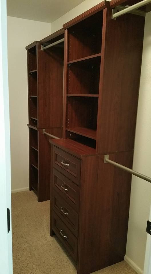 Dark wood closet organization system with shelving, four drawers, and hanging rods installed in a carpeted walk-in closet.