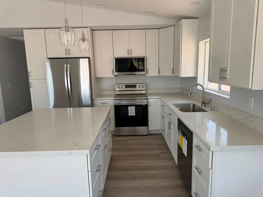 A modern kitchen featuring white cabinets, stainless steel appliances, an island with quartz countertops, and wood floors.
