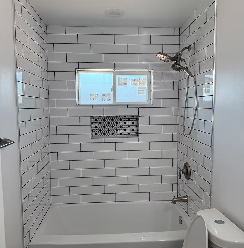 A white tiled shower and bathtub alcove featuring a window, a decorative black and white niche, and chrome fixtures.