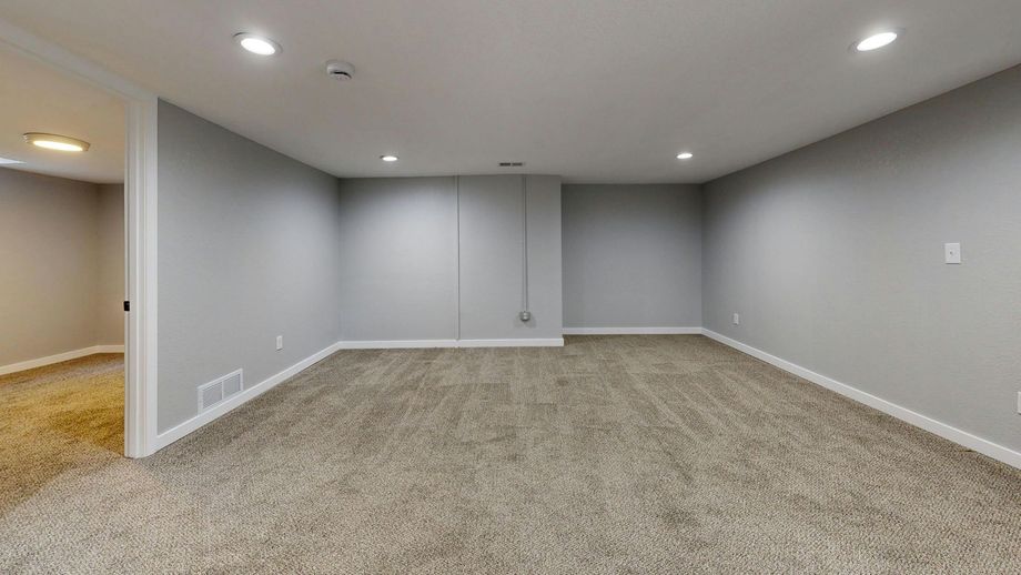 A finished basement with gray walls, white trim, recessed lighting, and patterned carpet, featuring an open doorway.