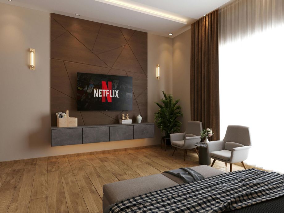 Modern bedroom with a wood-paneled wall, TV displaying Netflix, floating gray cabinets, two armchairs, and wood floors.