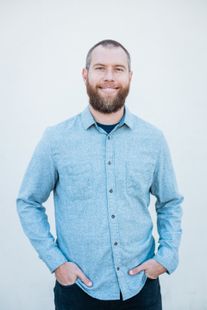 A man with a beard is wearing a plaid shirt and smiling for the camera.