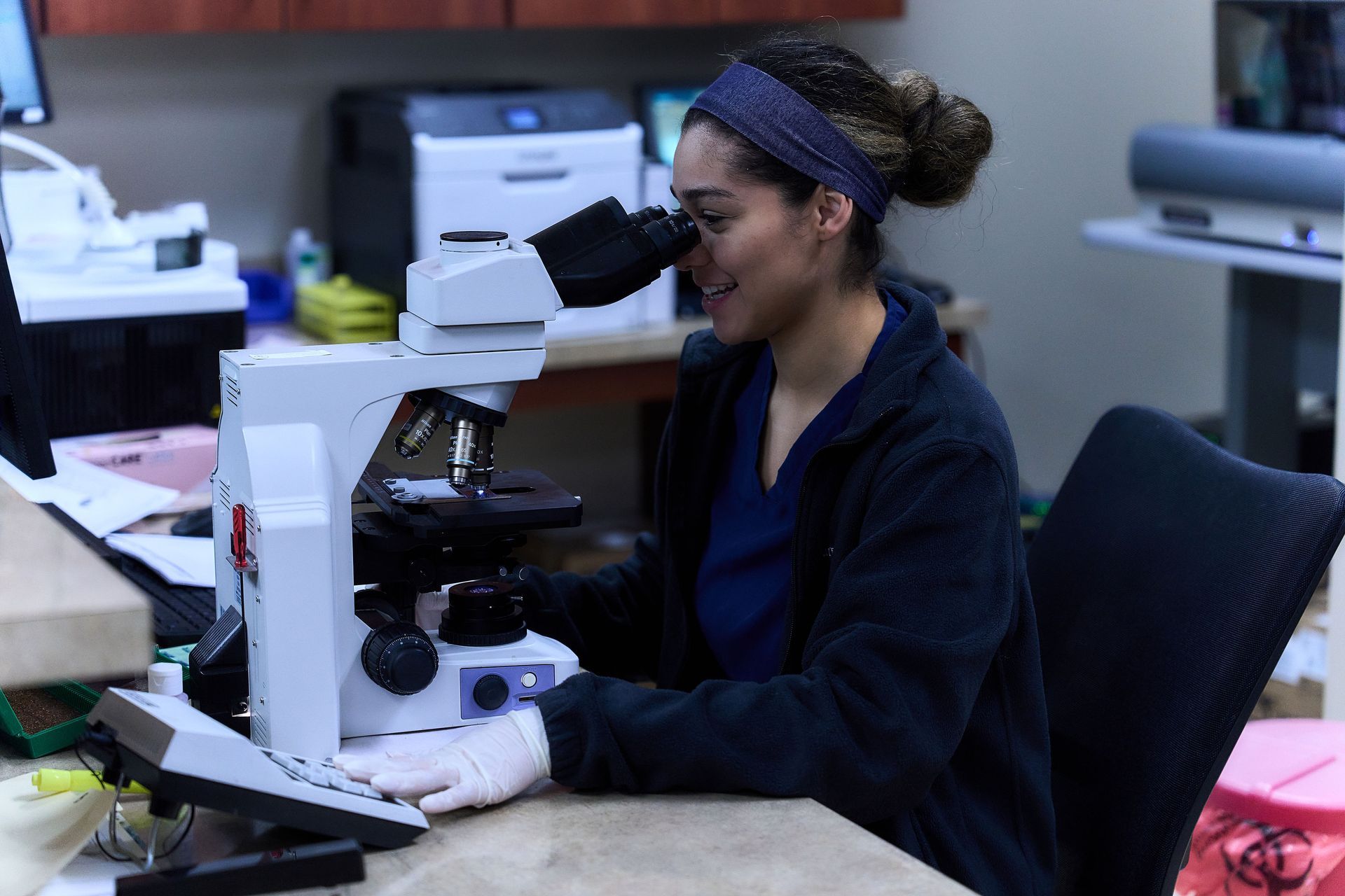 A woman is looking through a microscope in a lab.