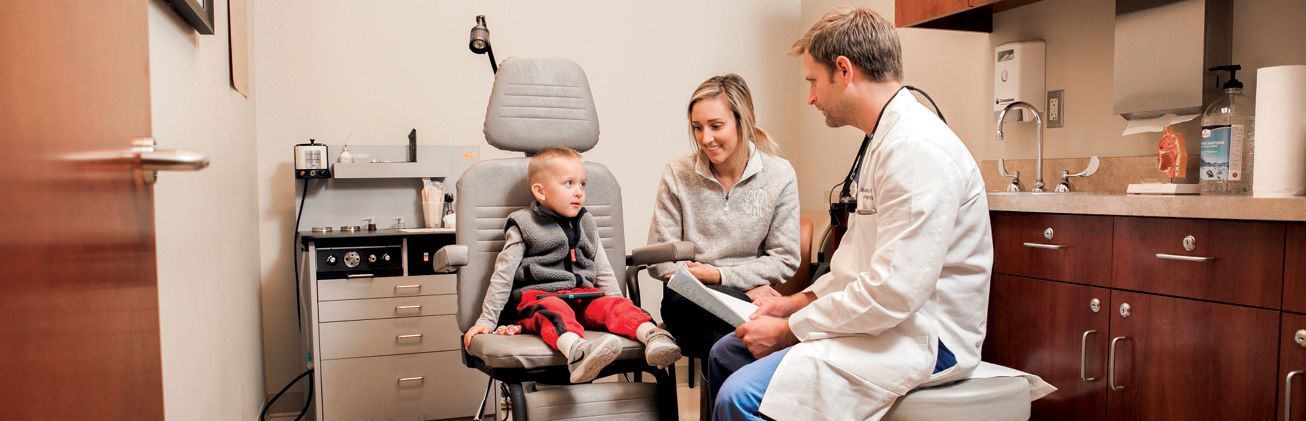 a little boy is sitting in a chair talking to a doctor