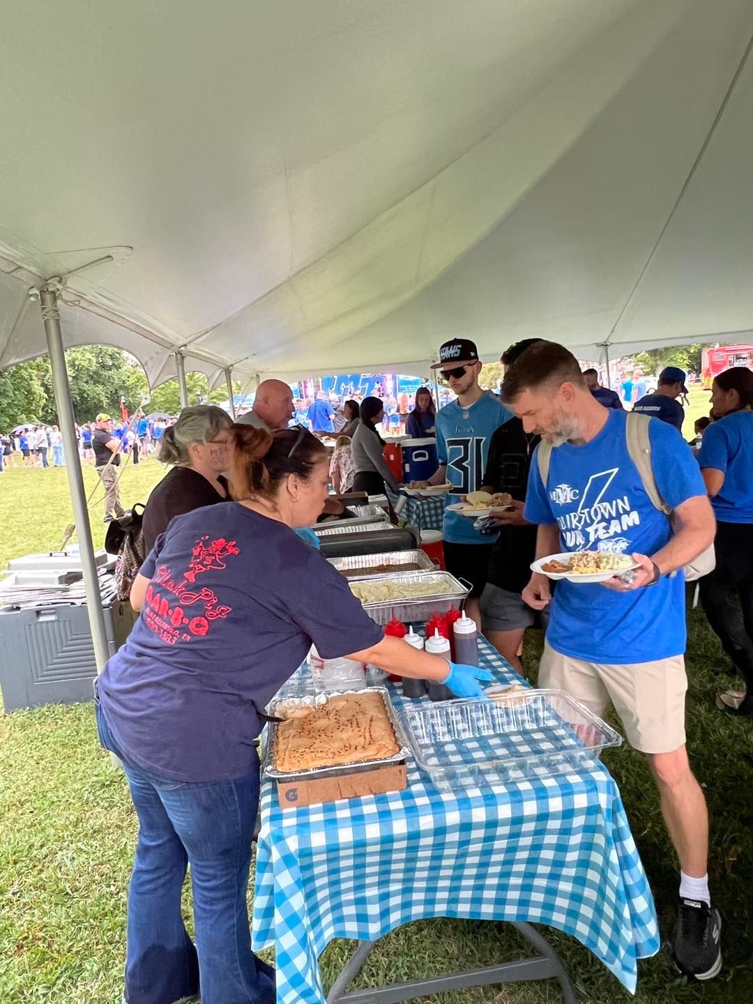A group of people are standing around a table under a tent eating food.
