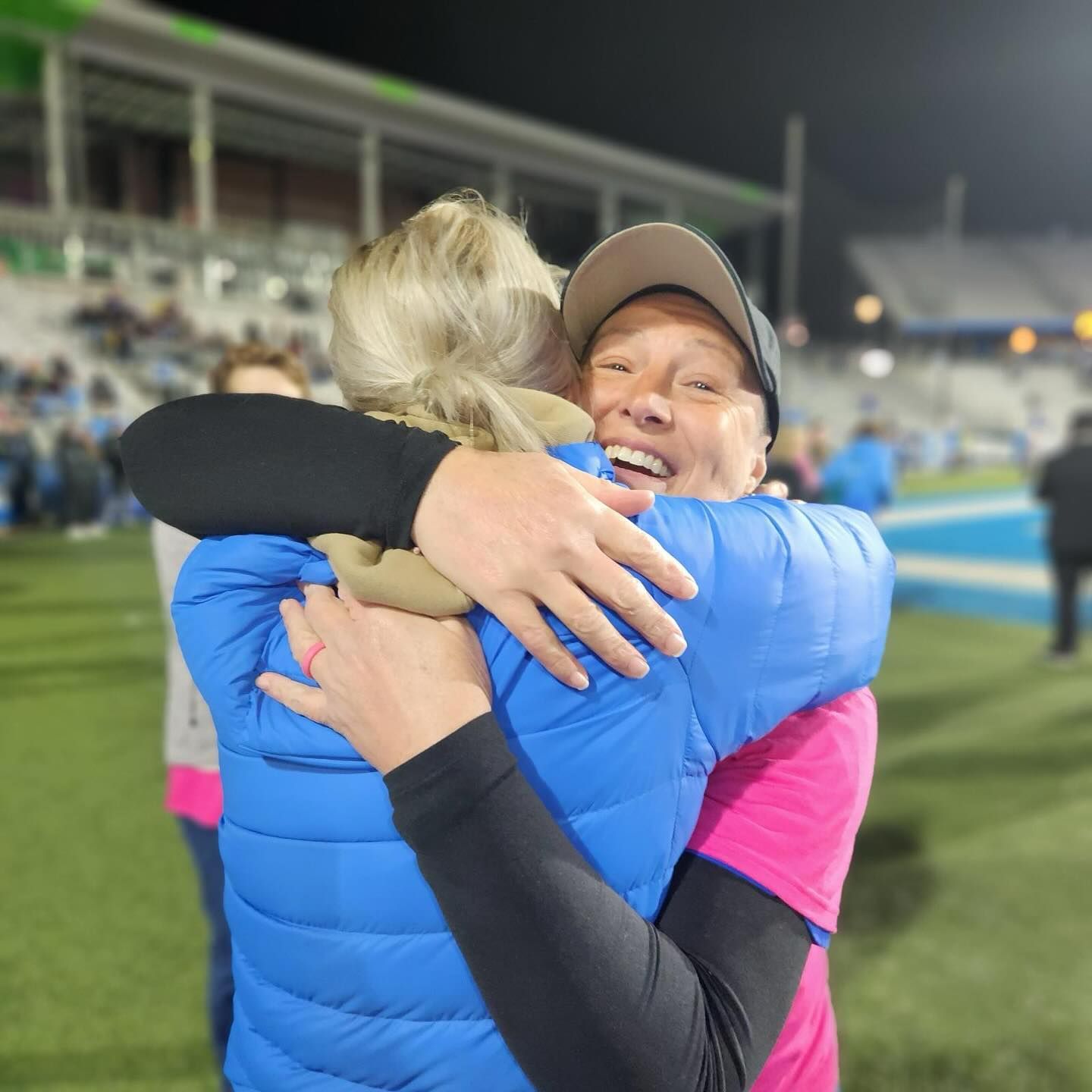 A woman in a blue vest is hugging another woman in a pink shirt