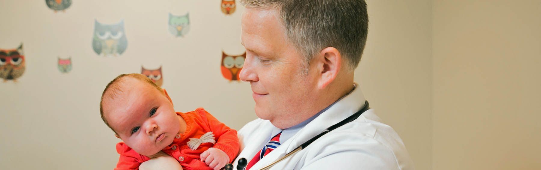 a doctor is holding a baby with owls on the wall behind him