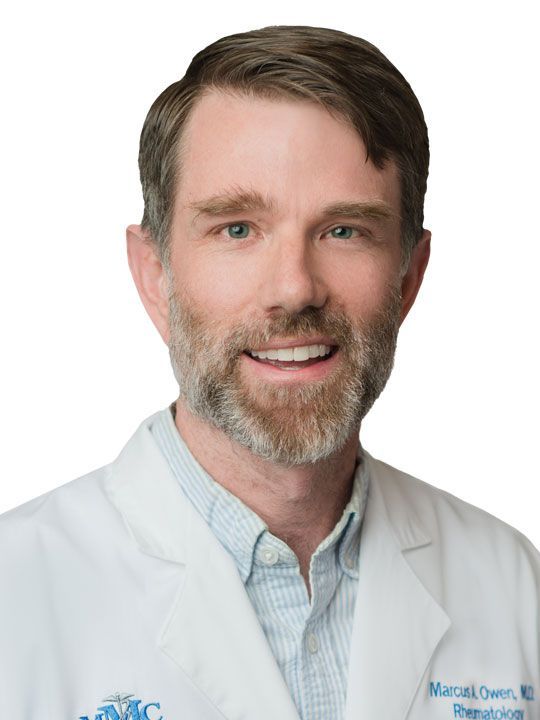 A man with a beard is wearing a white lab coat