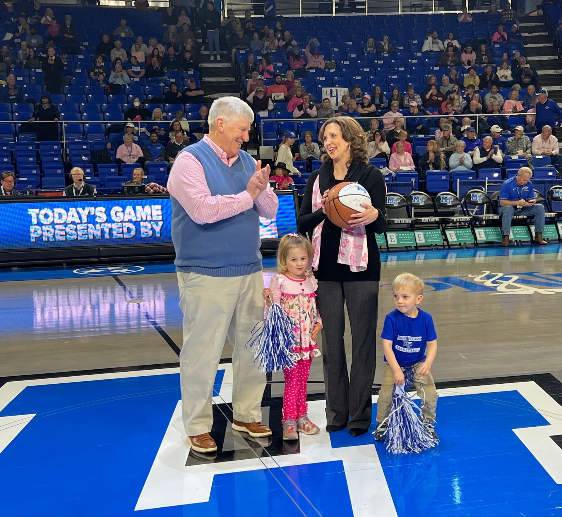 A group of people on a basketball court with a sign that says today 's game presented by