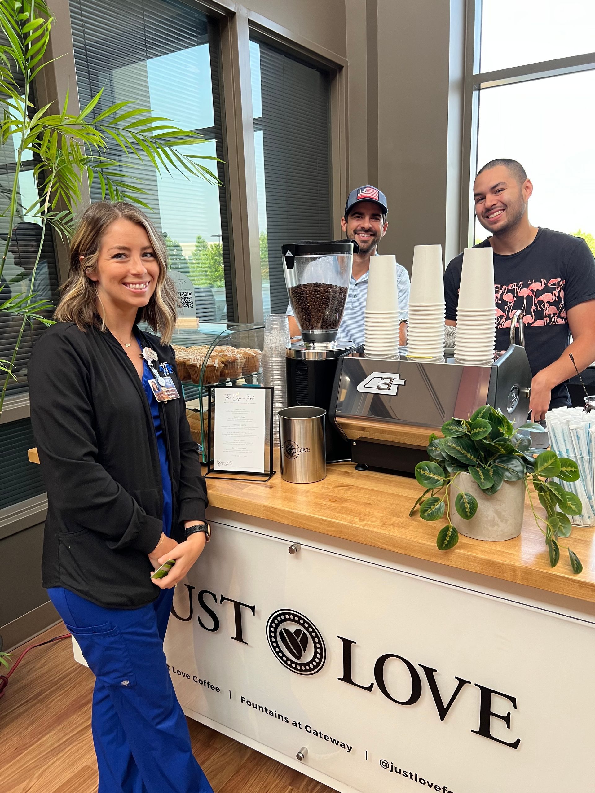 A woman and two men are standing in front of a counter that says just love.