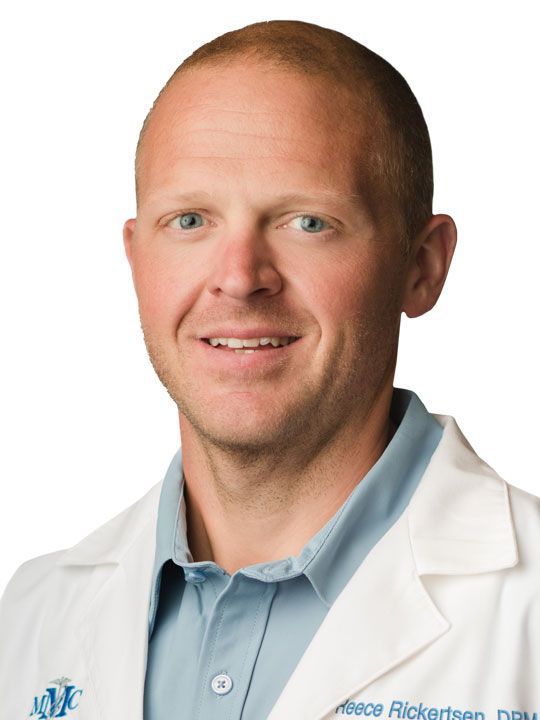 A man in a white lab coat and tie is smiling for the camera.