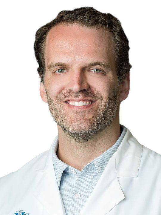 A man with a beard is wearing a white lab coat and smiling.