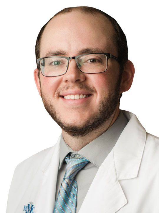 A man in a lab coat and tie is smiling for the camera.