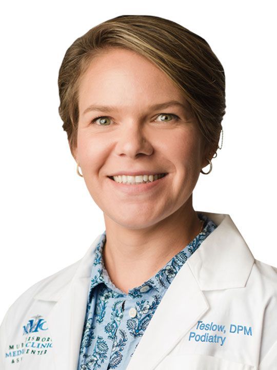 A man in a white lab coat and tie is smiling for the camera.
