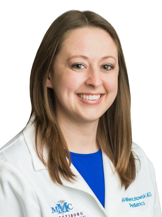 A woman wearing a white lab coat and a blue shirt is smiling.