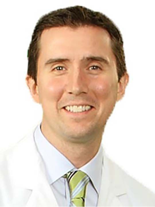 A man in a white coat and tie is smiling for the camera.