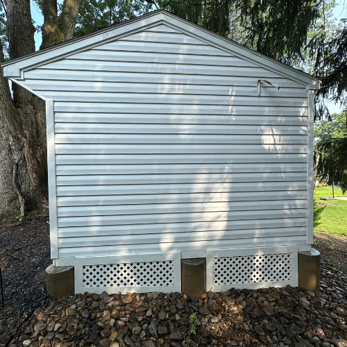 A white shed is sitting on top of a pile of rocks.