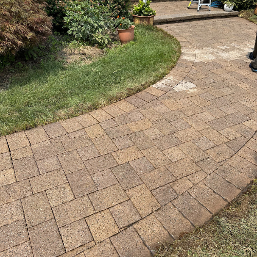 A brick walkway leading to a patio in a backyard.