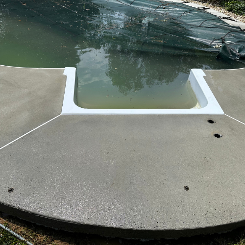 A concrete deck next to a swimming pool with a hole in it