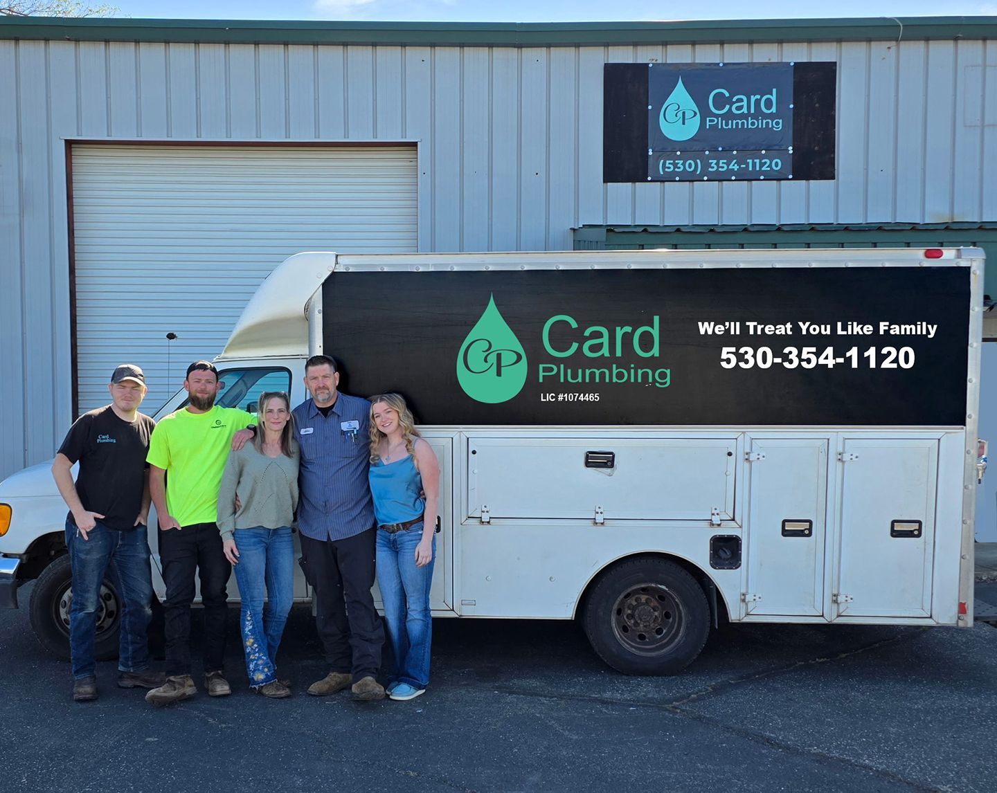 A group of five people posing in front of a white Card Plumbing utility truck parked outside a workshop.