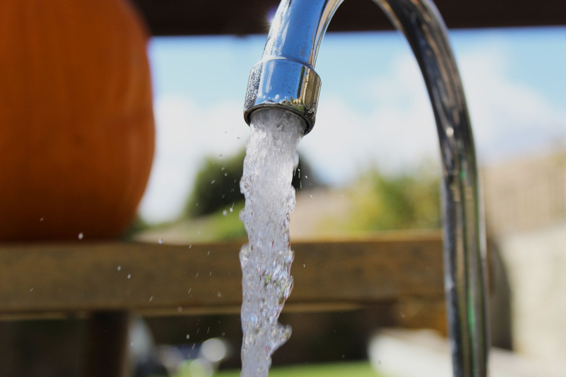 A close-up view of a metal faucet pouring a steady stream of clear water against an out-of-focus background.