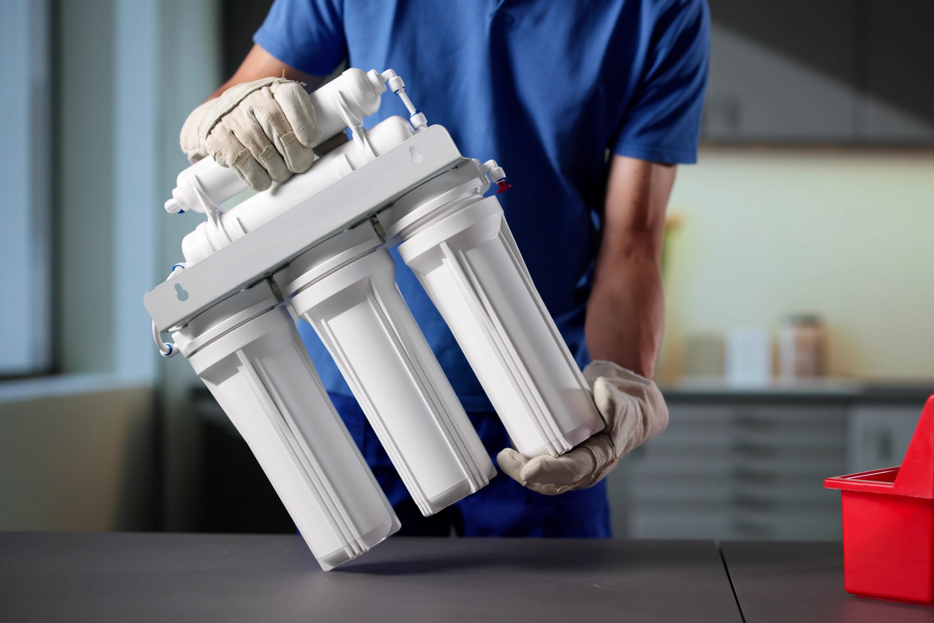 A person in a blue shirt and gloves holds a multi-stage water filtration system assembly on a table.