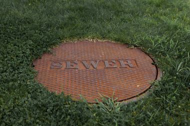 Orange sewer manhole cover in grass with “SEWER” embossed on top