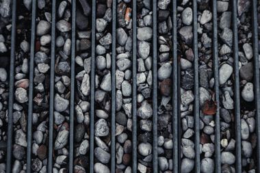 Vertical metal bars over gray stones and pebbles, with a few darker rocks mixed in