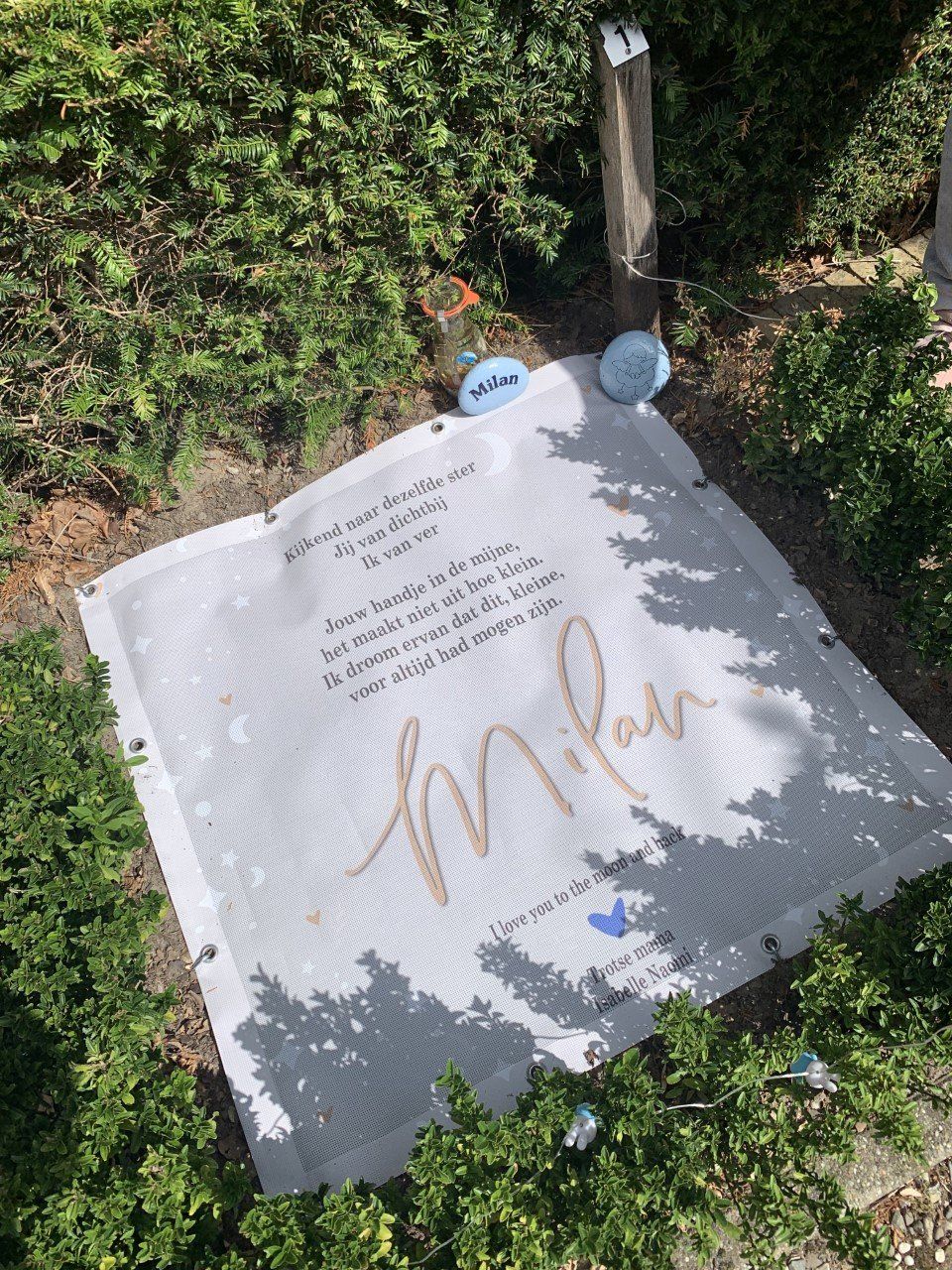 Tijdelijk grafdoek. Op de grond ligt een witte deken met de naam Milaan erop geschreven.