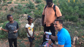 A man in a blue shirt is kneeling down next to a group of children in a field.