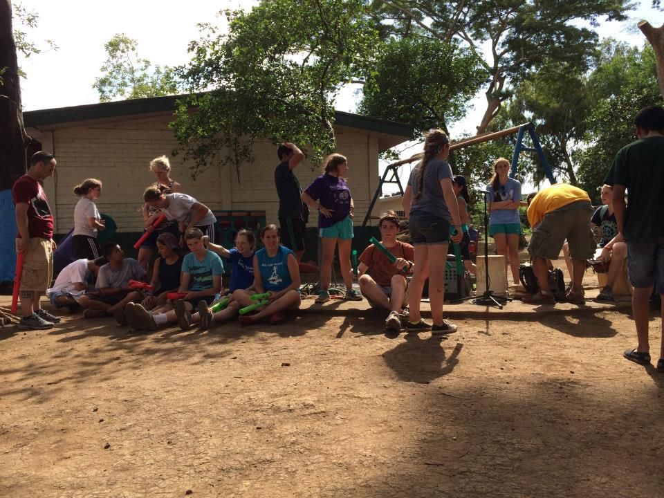 A group of people are sitting on the ground in front of a building.