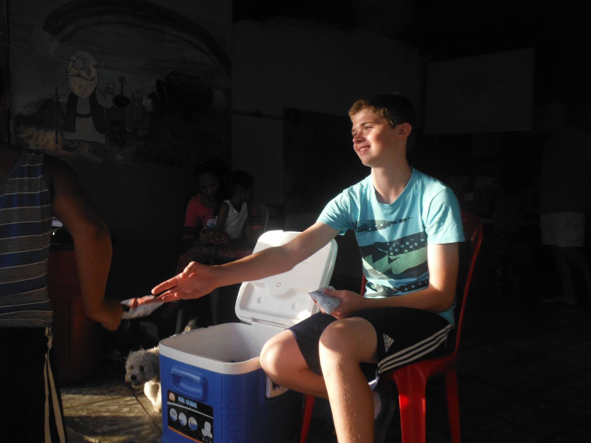 A young man is sitting in a chair next to a blue cooler.