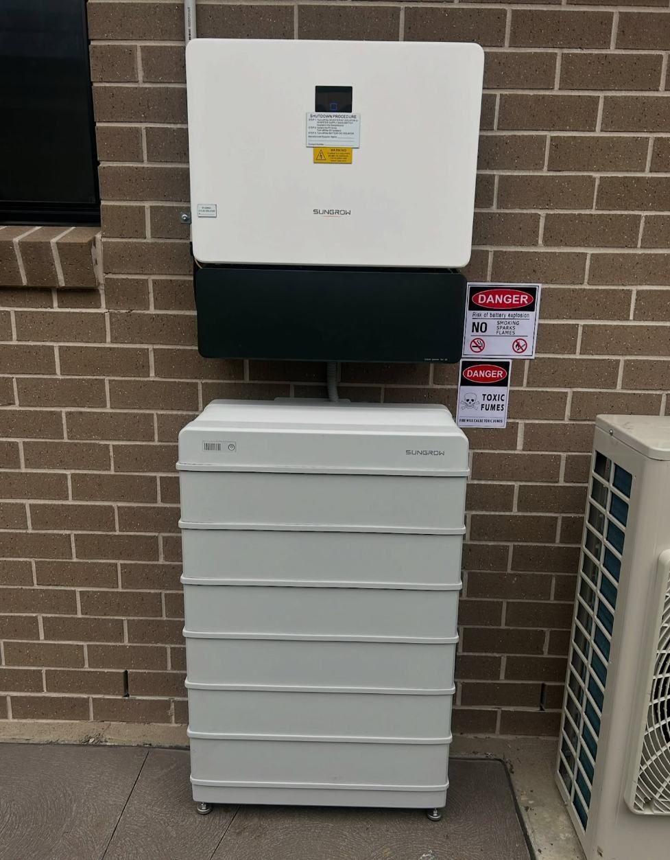A White Battery Box is Sitting in Front of a Brick Wall — DLG Electrical & Solar In Hunter Valley, NSW