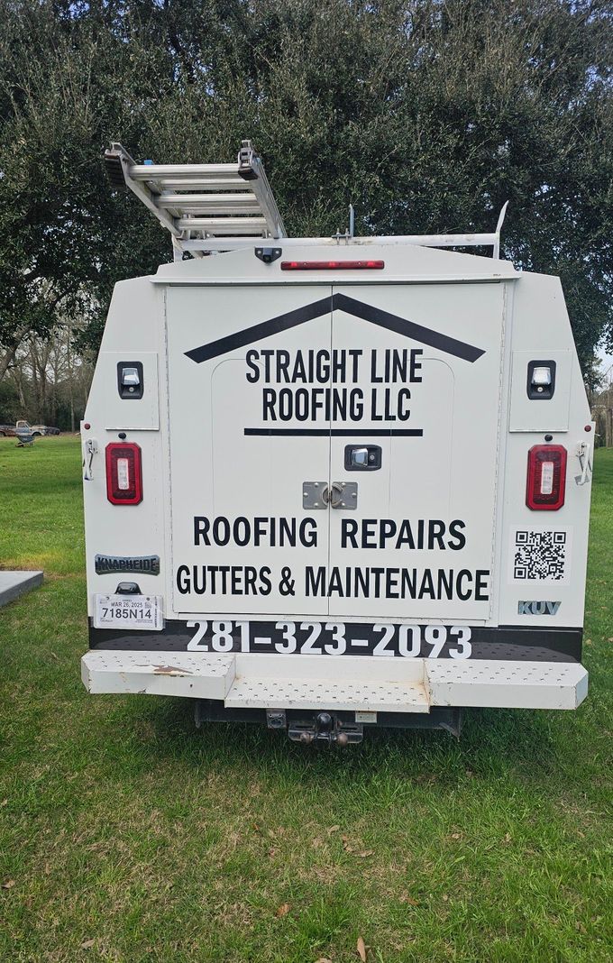 A white truck with a ladder on top of it is parked in a grassy field.