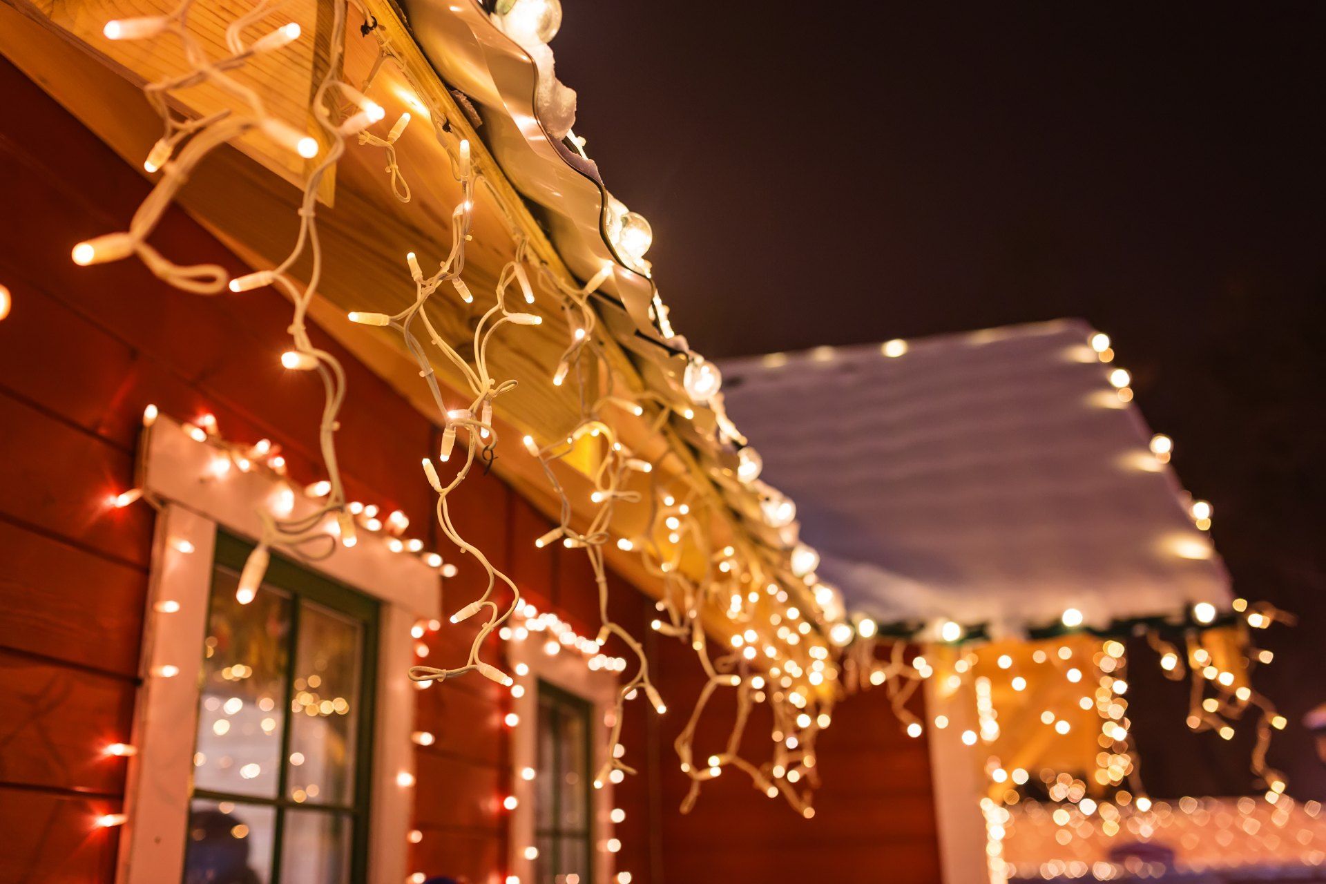 Christmas lights are hanging from the roof of a red house.