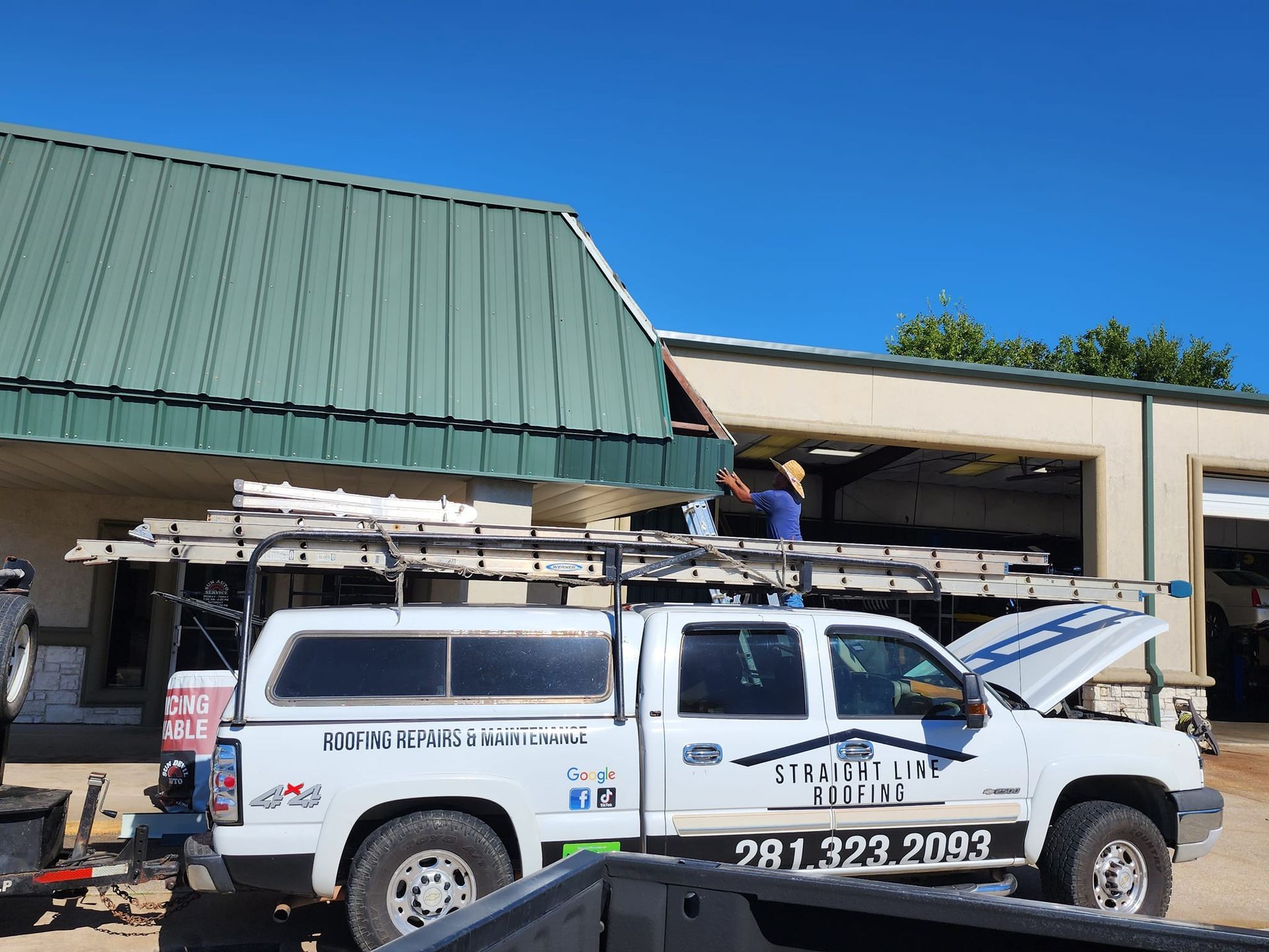 A white truck with the hood open is parked in front of a building.