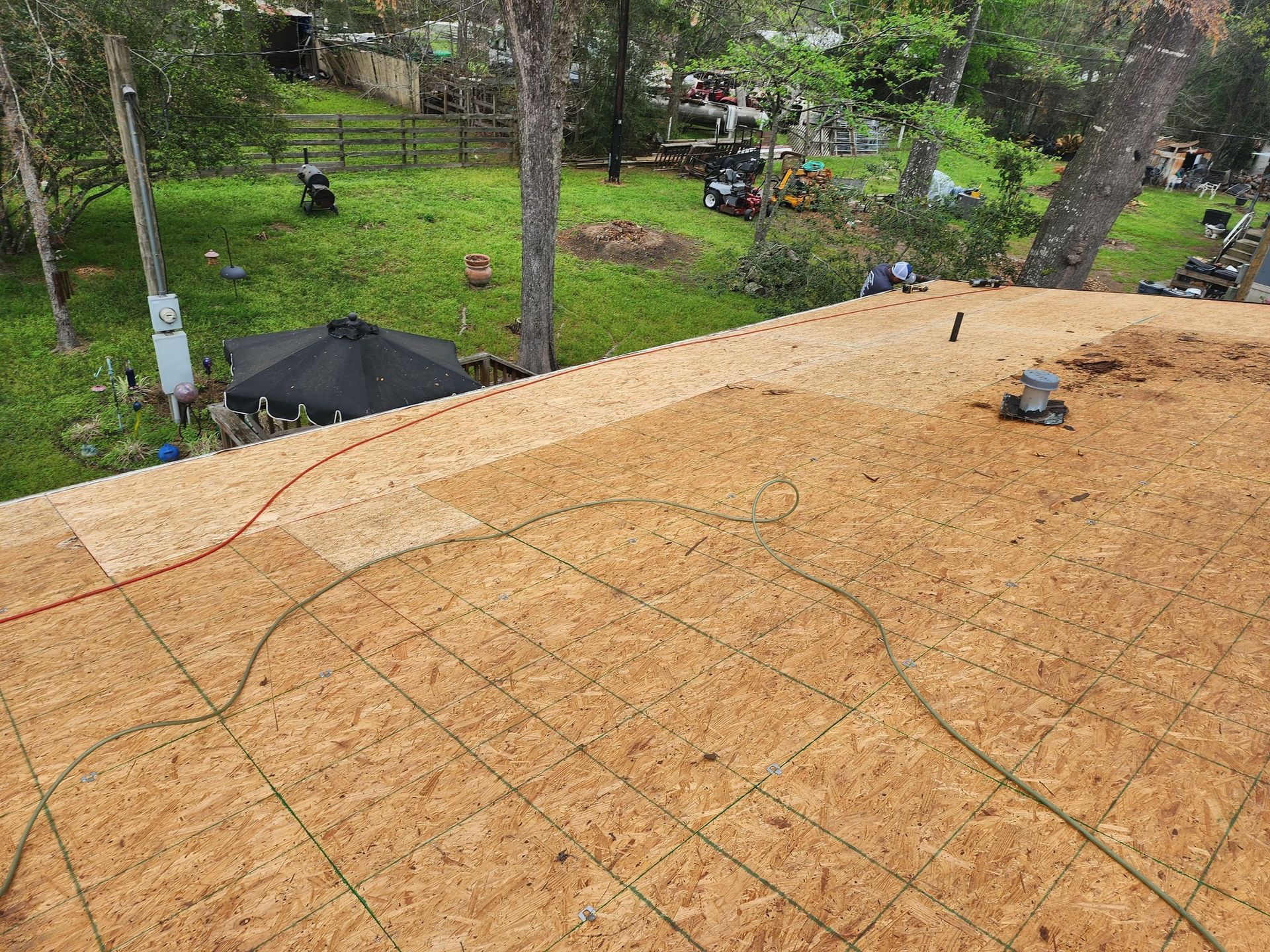 A roof is being built in a backyard with trees in the background.