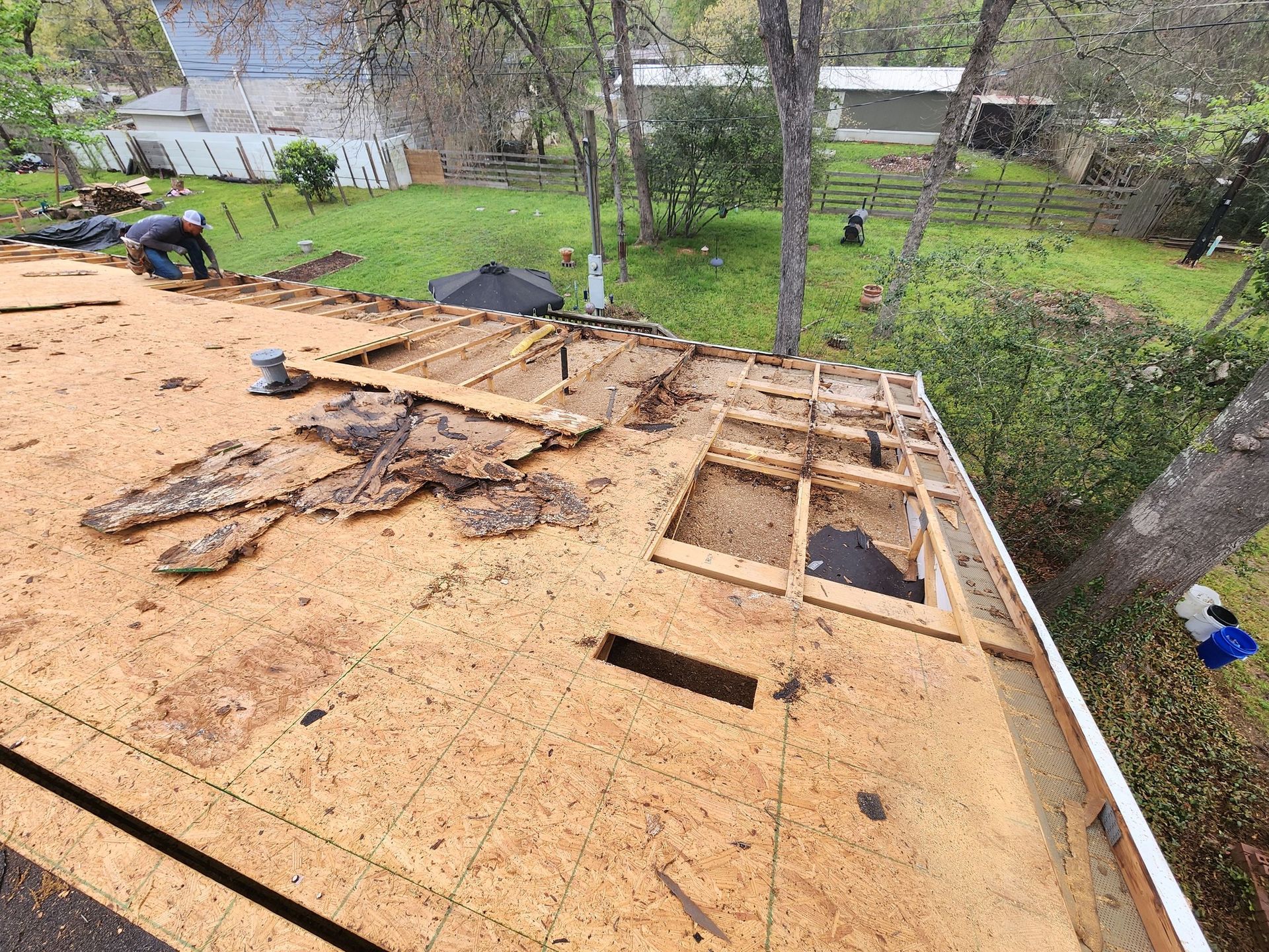 A roof is being repaired in a backyard with trees in the background.