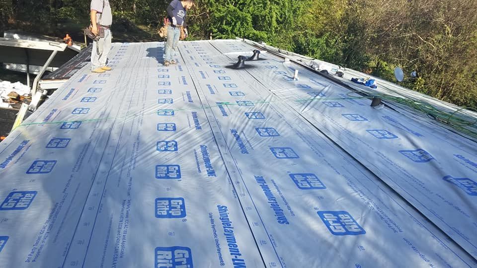 A man is standing on top of a roof covered in a roofing material.