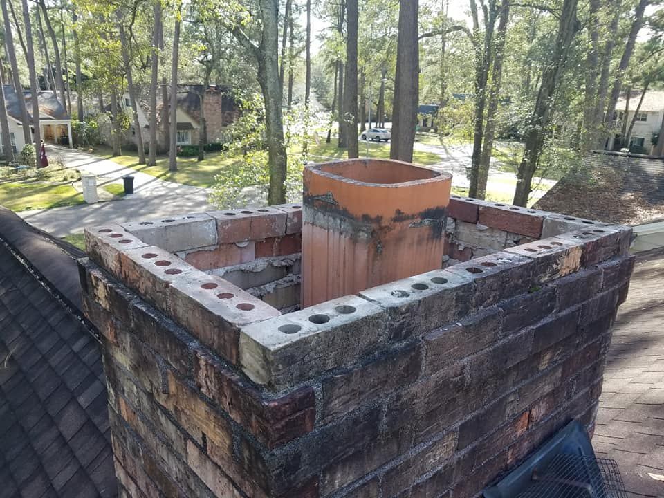 A brick chimney on top of a roof with trees in the background.