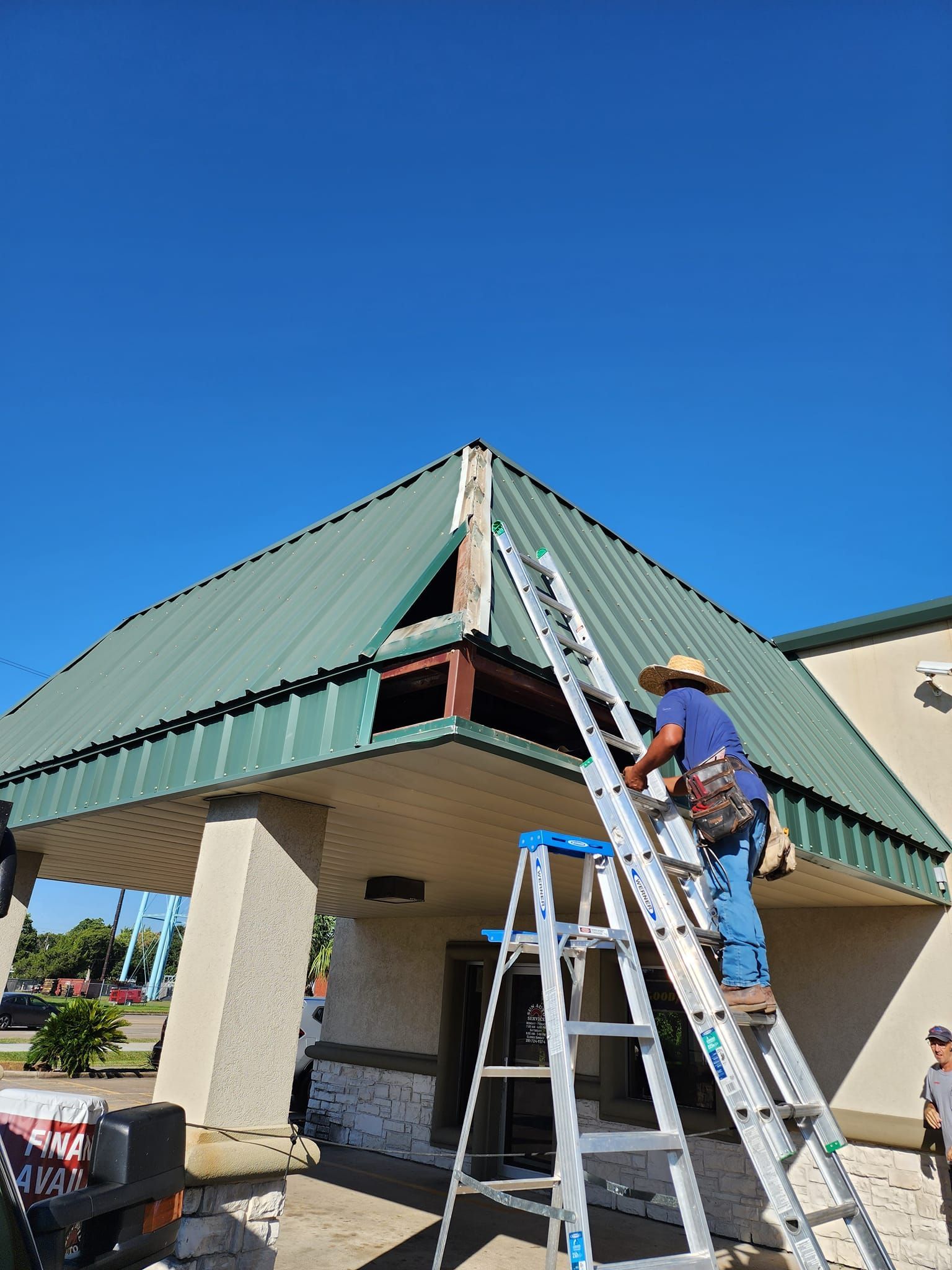 A man is standing on a ladder working on the roof of a building.