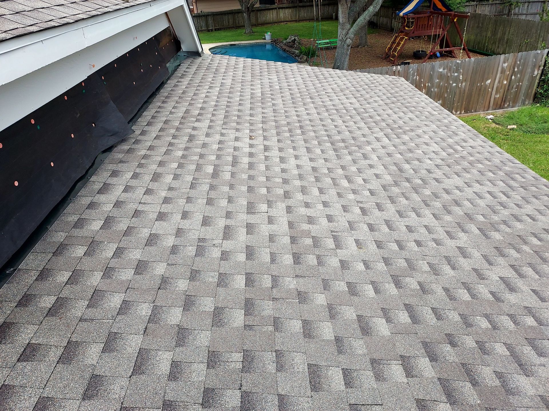 The roof of a house with a pool in the background.