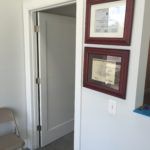 A room with a chair , a door , and three framed pictures on the wall.