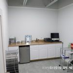 A kitchen with white cabinets , a dishwasher , a computer and a desk.