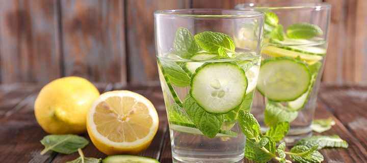 Two glasses of water with cucumber , lemon and mint on a wooden table.