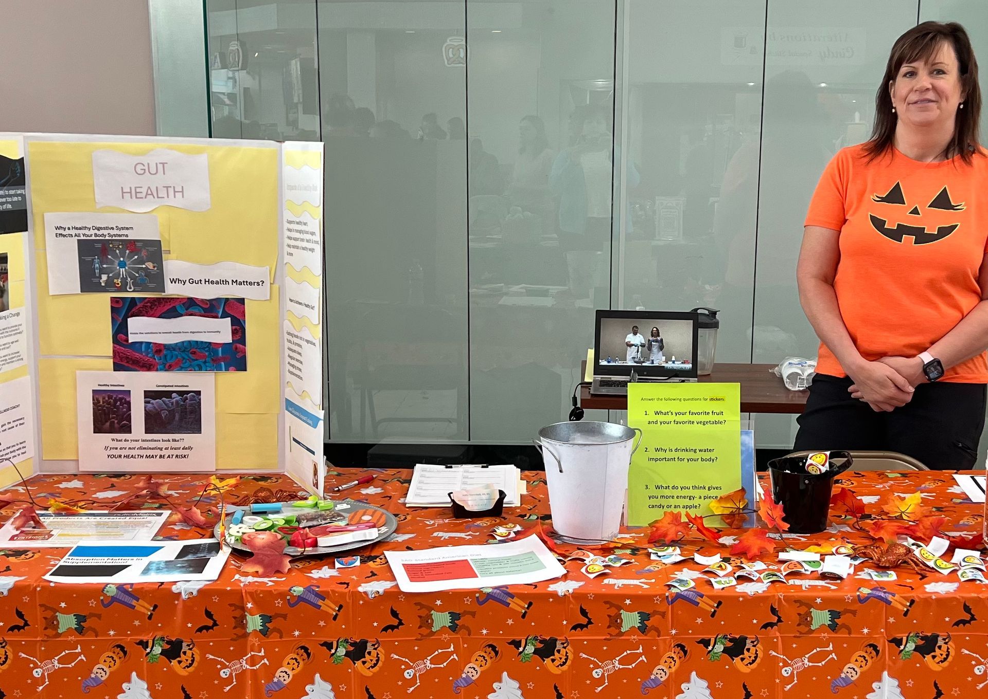 A woman in an orange shirt is standing in front of a table with a pumpkin on it.