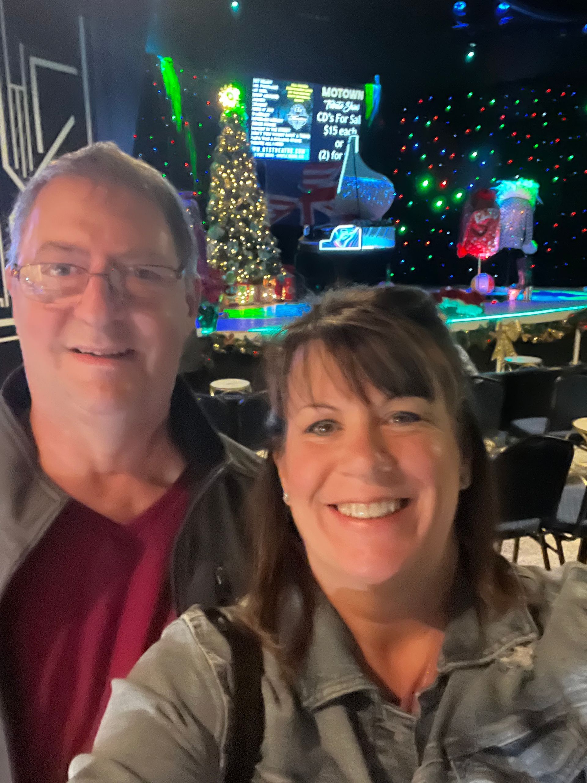 A man and a woman are posing for a picture in front of a christmas tree.